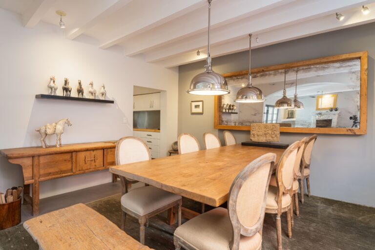 Rustic dining room with a long wooden table, upholstered chairs, and horse figurines on a shelf against a white wall, San Miguel de Allende