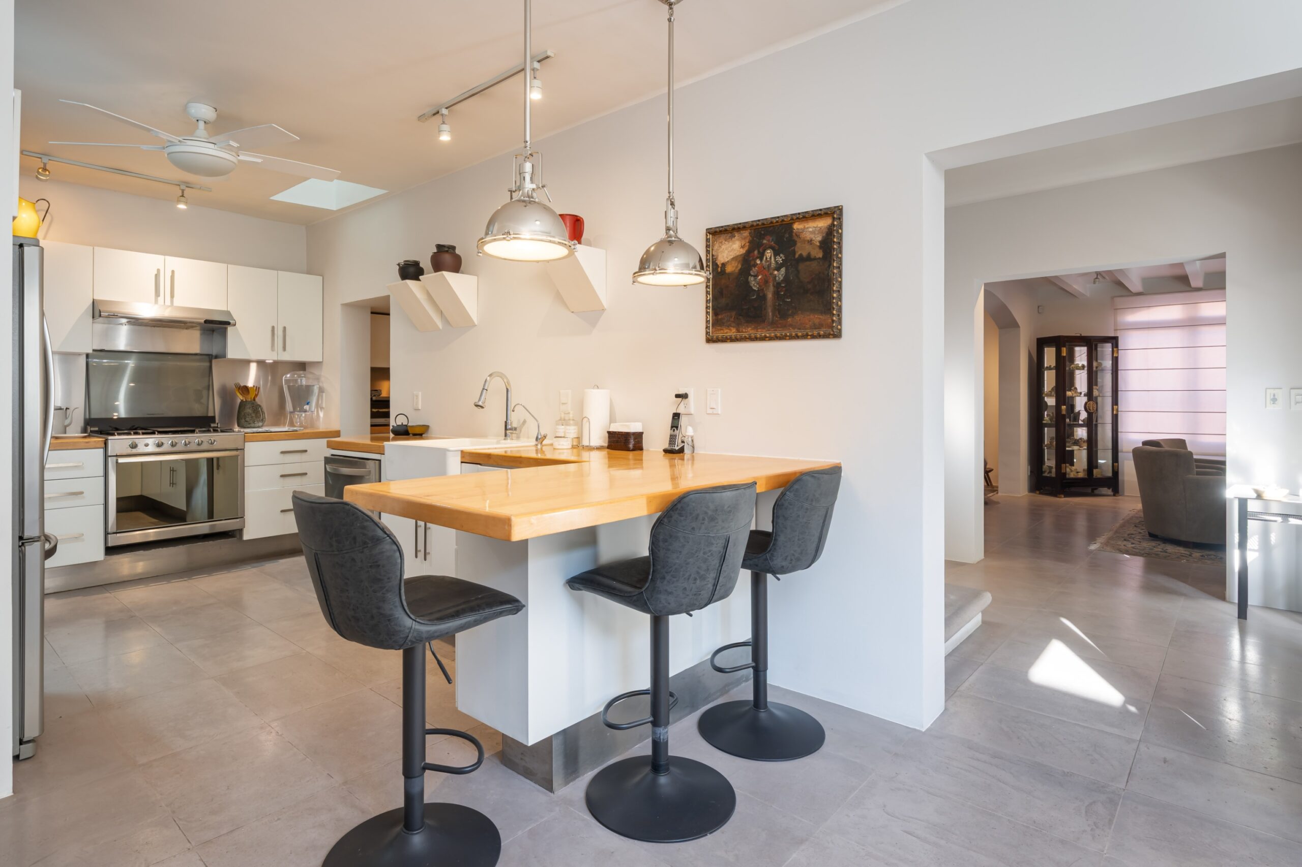 Open-concept kitchen with stainless steel appliances, white cabinets, a wooden island, and four black bar stools, San Miguel de Allende