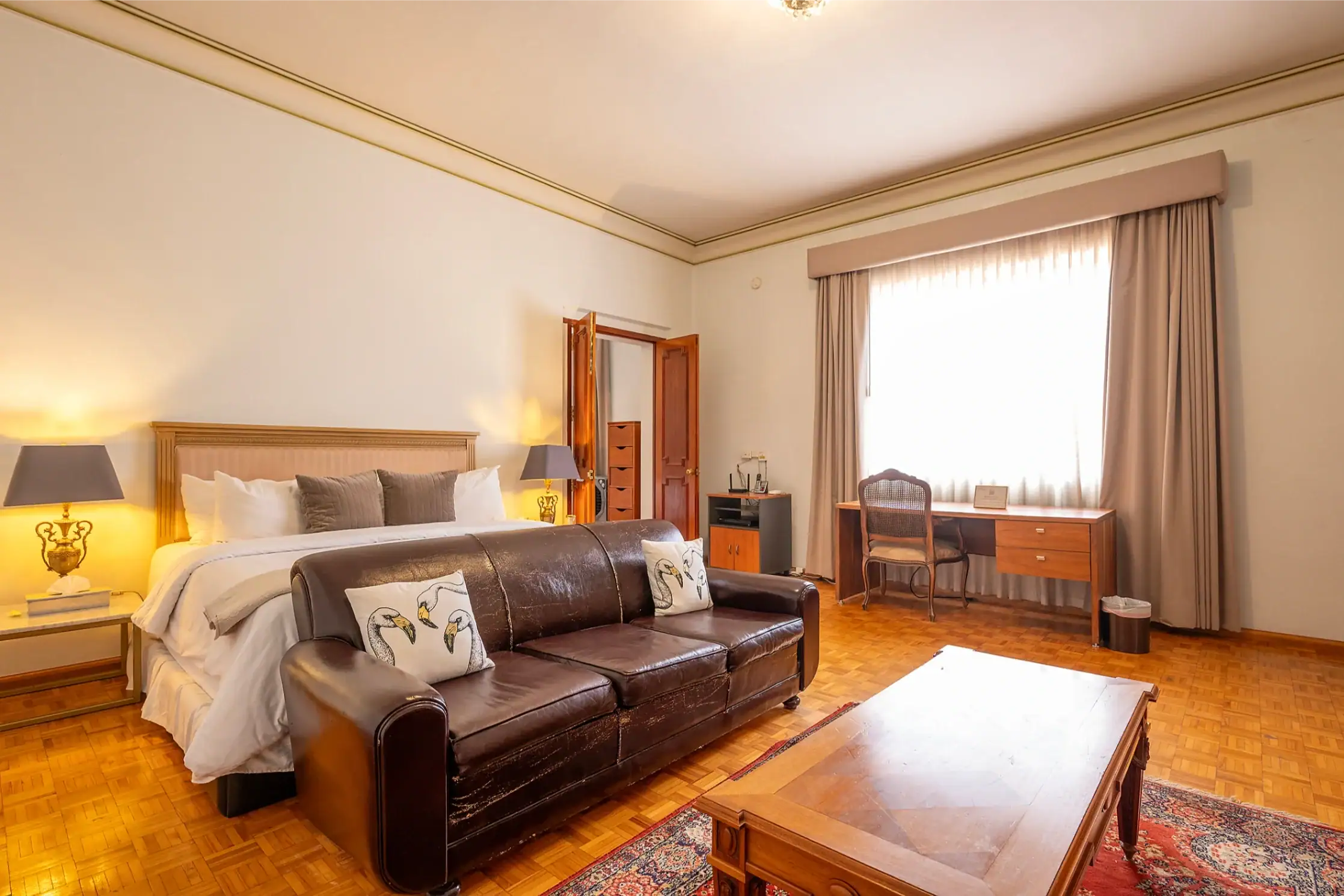 Hotel bedroom with king bed, leather sofa, and beige curtains by a large window, San Miguel de Allende
