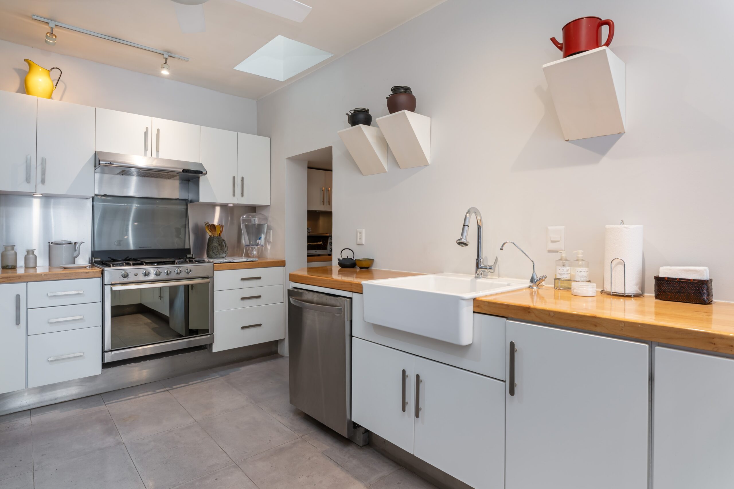 Bright, modern kitchen with white cabinets, stainless steel oven, and wood countertops; decorative pots on angled wall shelves, San Miguel de Allende
