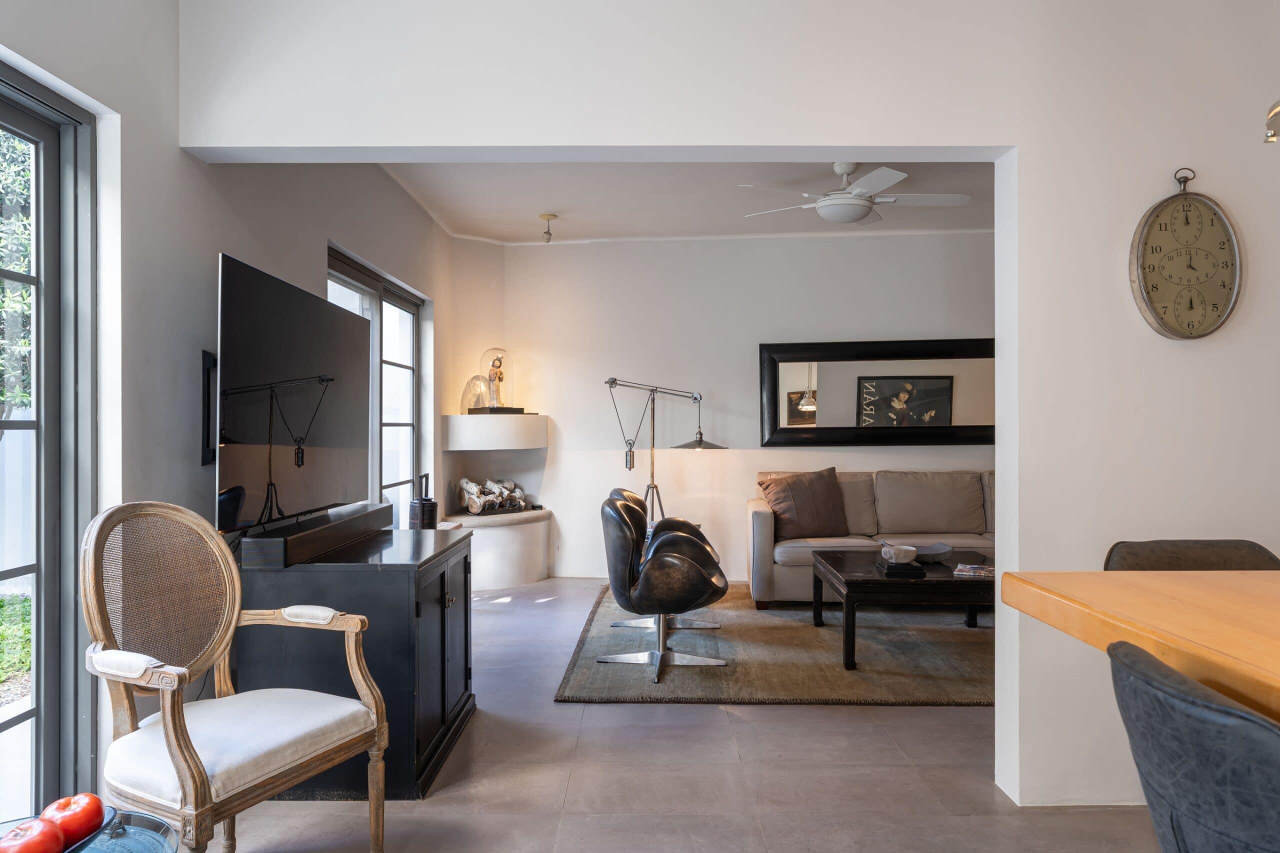 Open living room with light gray walls, beige sofa, black coffee table, wall clock, and a TV mounted on the wall, San Miguel de Allende