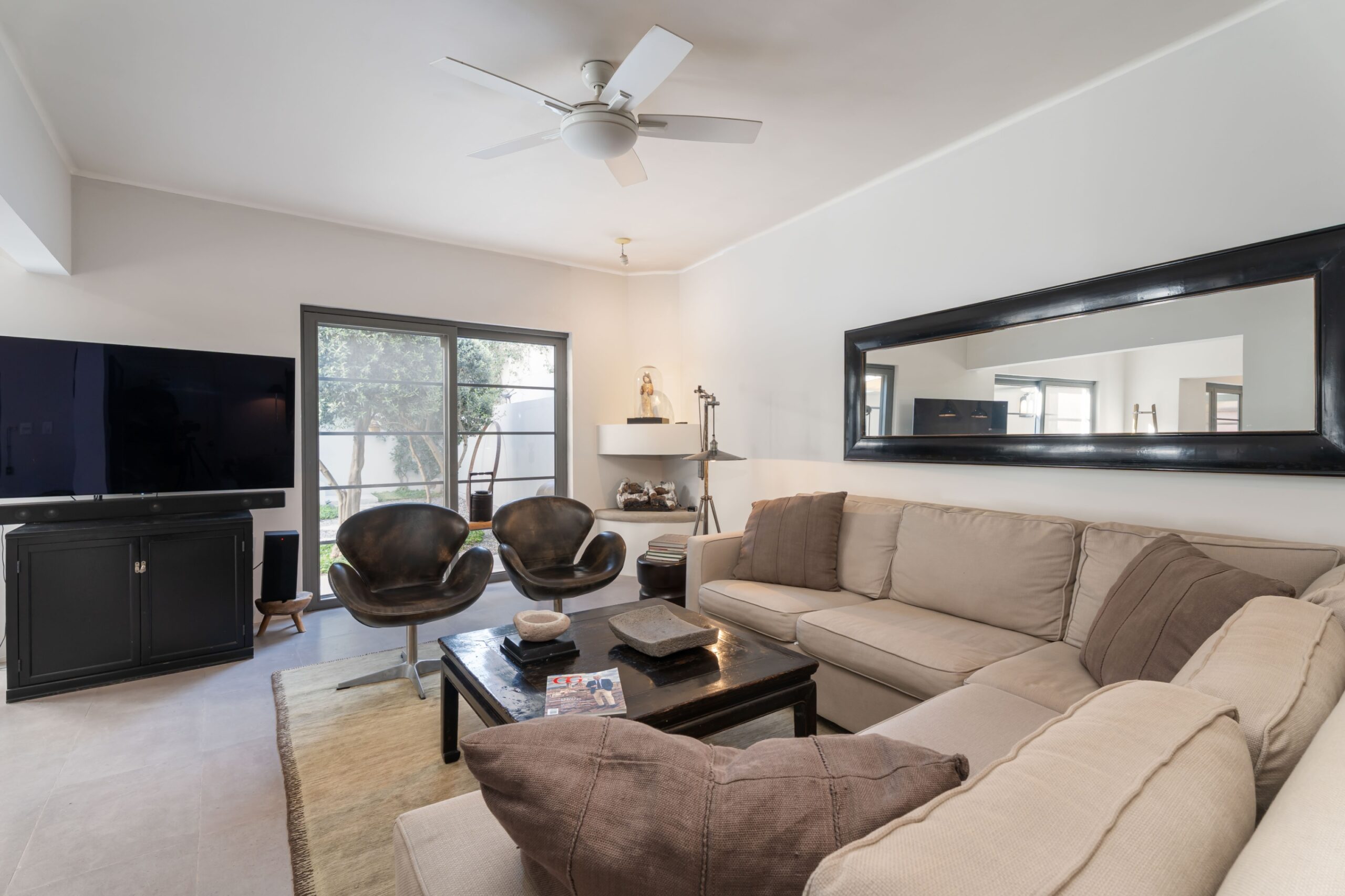 Bright modern living room with a beige sectional sofa, black coffee table, and a large horizontal mirror on the wall, San Miguel de Allende