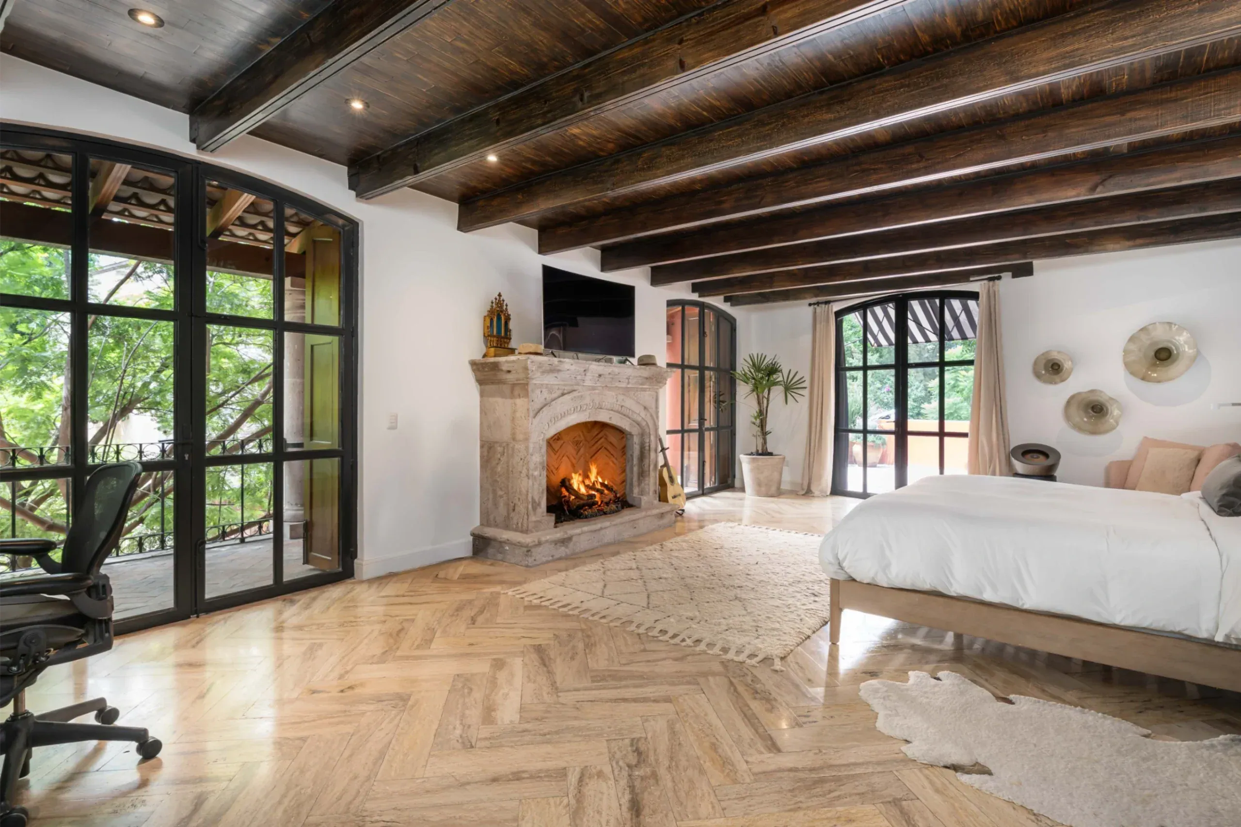 Casa Santa Mónica, primary bedroom with a stone fireplace and steel-framed doors, San Miguel de Allende