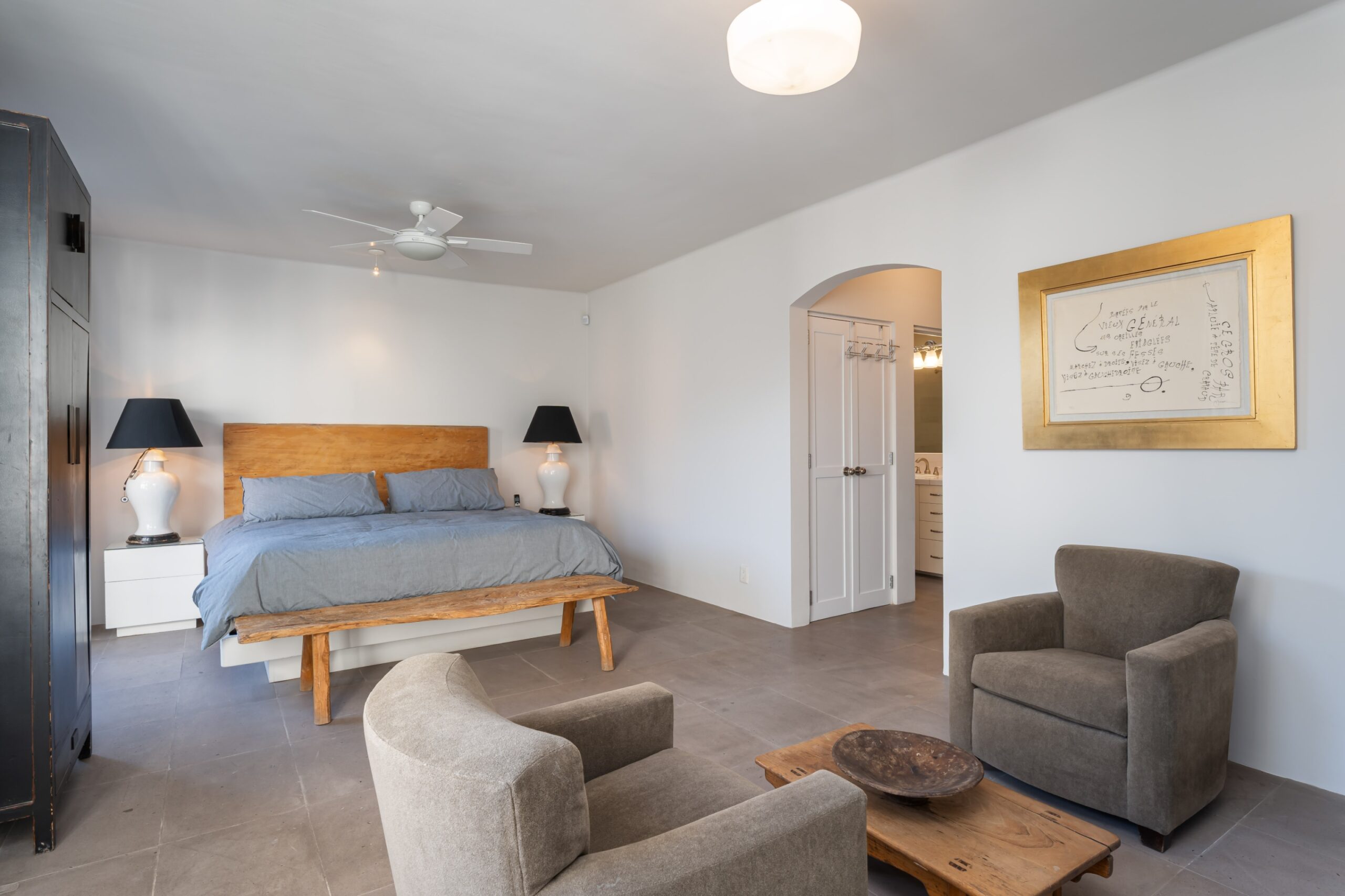 Modern bedroom with gray walls, wooden bed frame, blue-gray bedding, and matching nightstands with lamps on either side, San Miguel de Allende