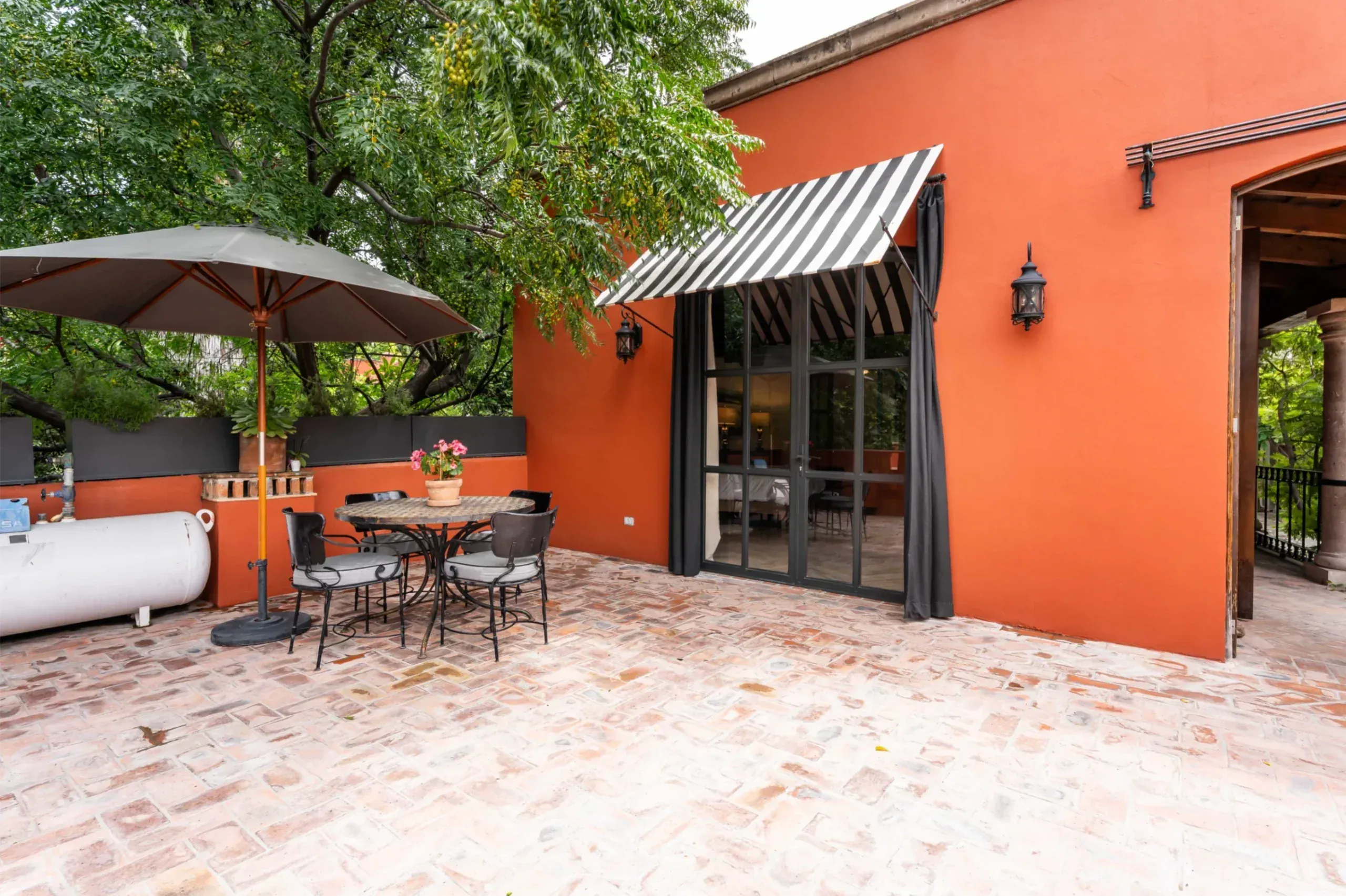 Casa Santa Mónica, brick terrace with a patio table, an umbrella and an orange wall, San Miguel de Allende