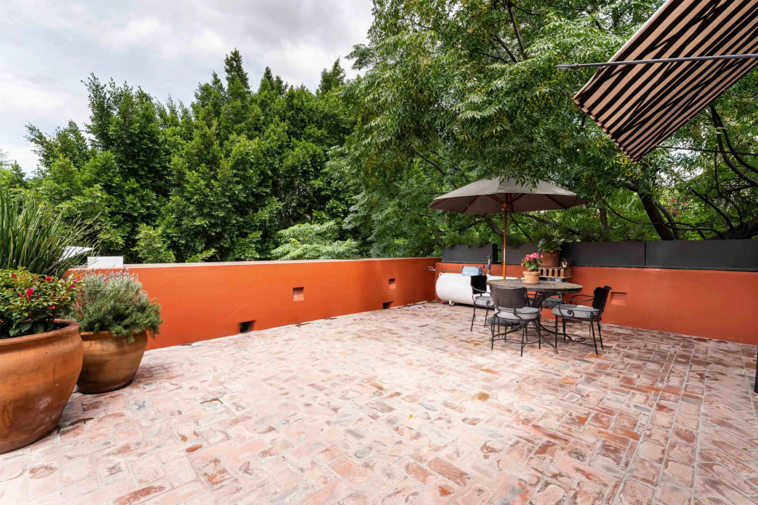 Casa Santa Mónica, brick terrace with an umbrella and an awning over steel-framed doors, San Miguel de Allende