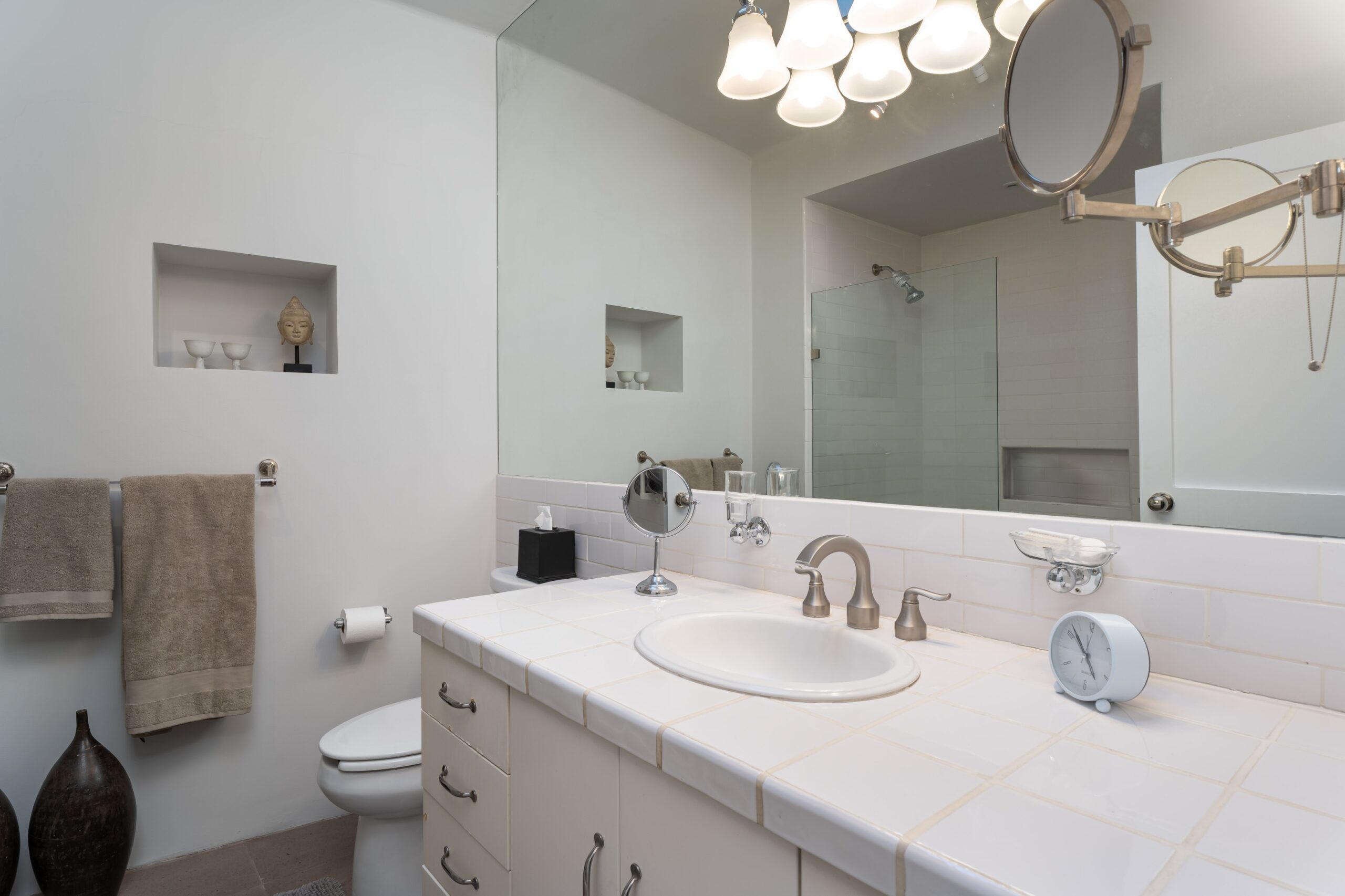 Bright bathroom vanity with dual sinks, white tile countertop, and a small clock on the counter beneath a large mirror, San Miguel de Allende
