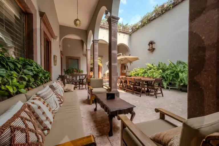 Sunlit covered patio with arched columns, beige seating, and leafy plants surrounding a courtyard dining area, San Miguel de Allende