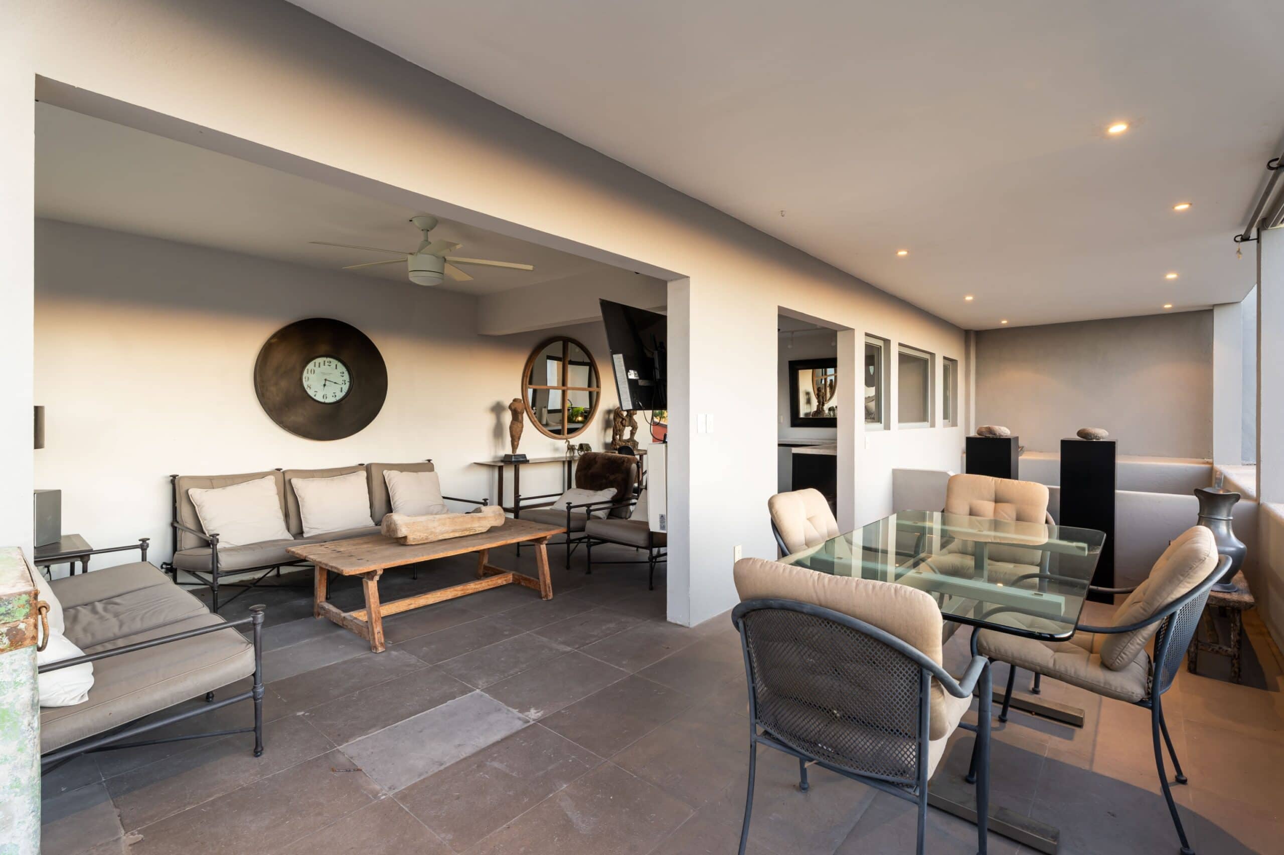 Covered outdoor living area with beige cushioned seating, a rustic wooden coffee table, and a ceiling fan above, San Miguel de Allende