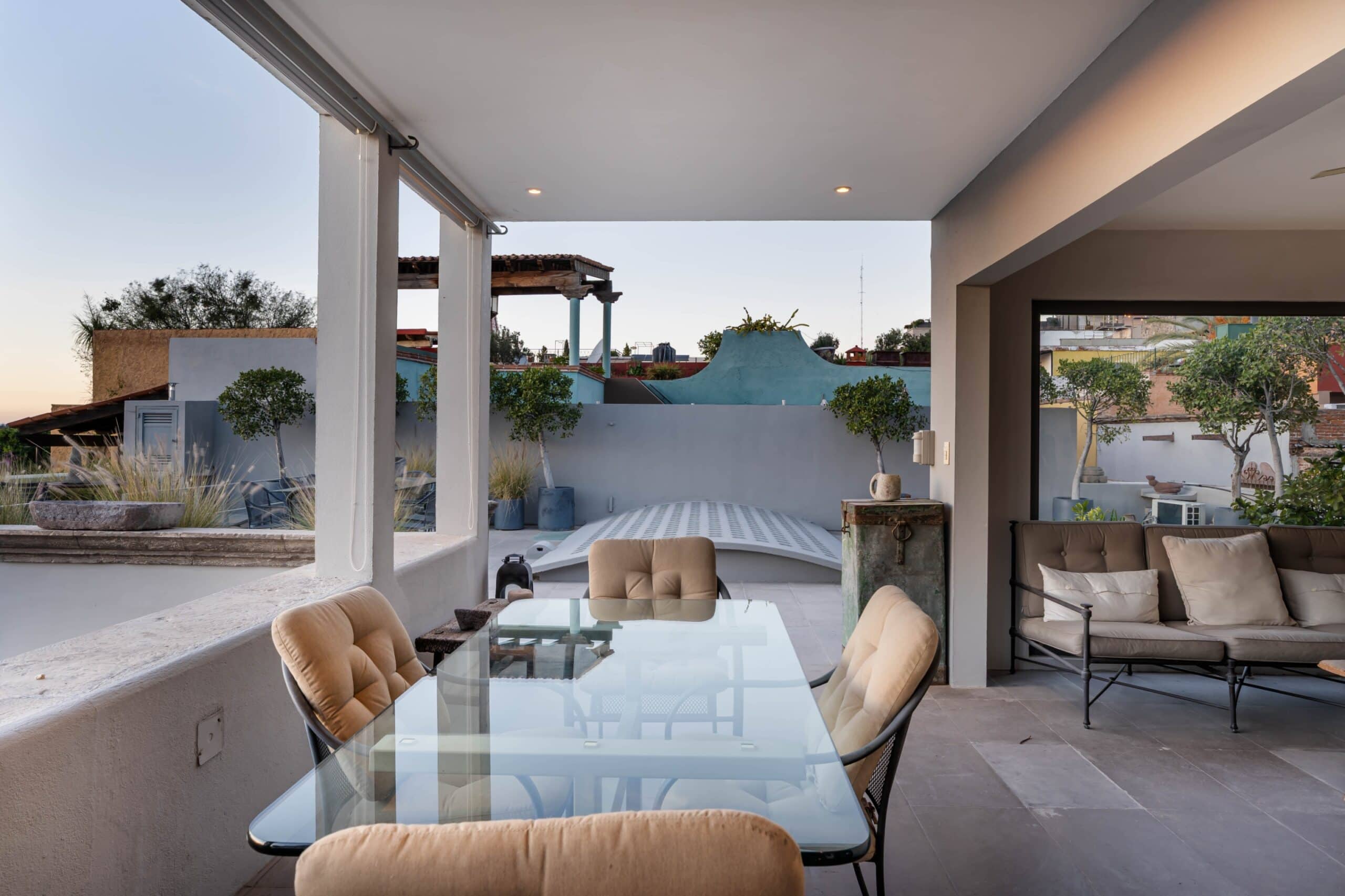 Outdoor patio with a glass dining table and tan cushioned chairs under a covered ceiling, San Miguel de Allende
