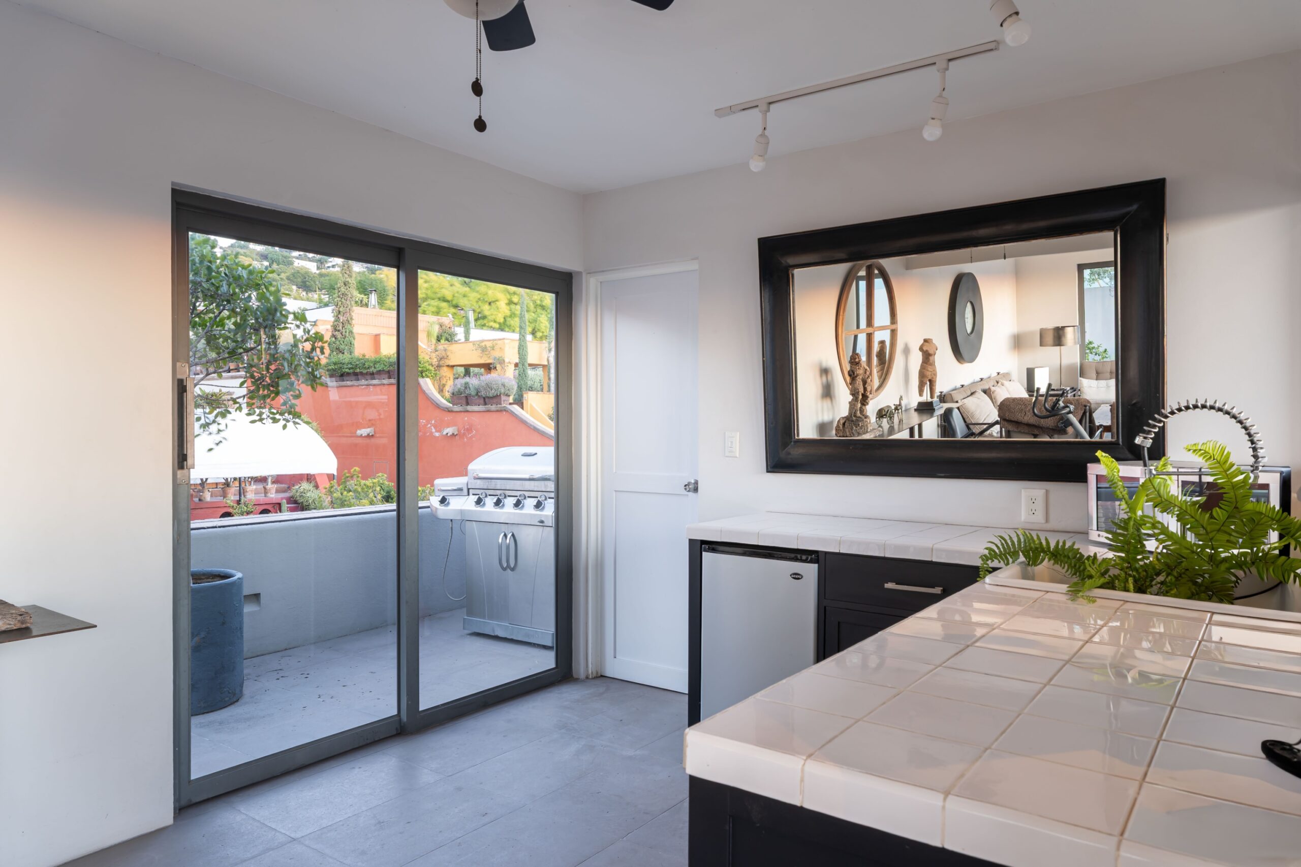 Modern kitchen with white tiled island, dark cabinets, and a sliding glass door leading to an outdoor grilling area, San Miguel de Allende