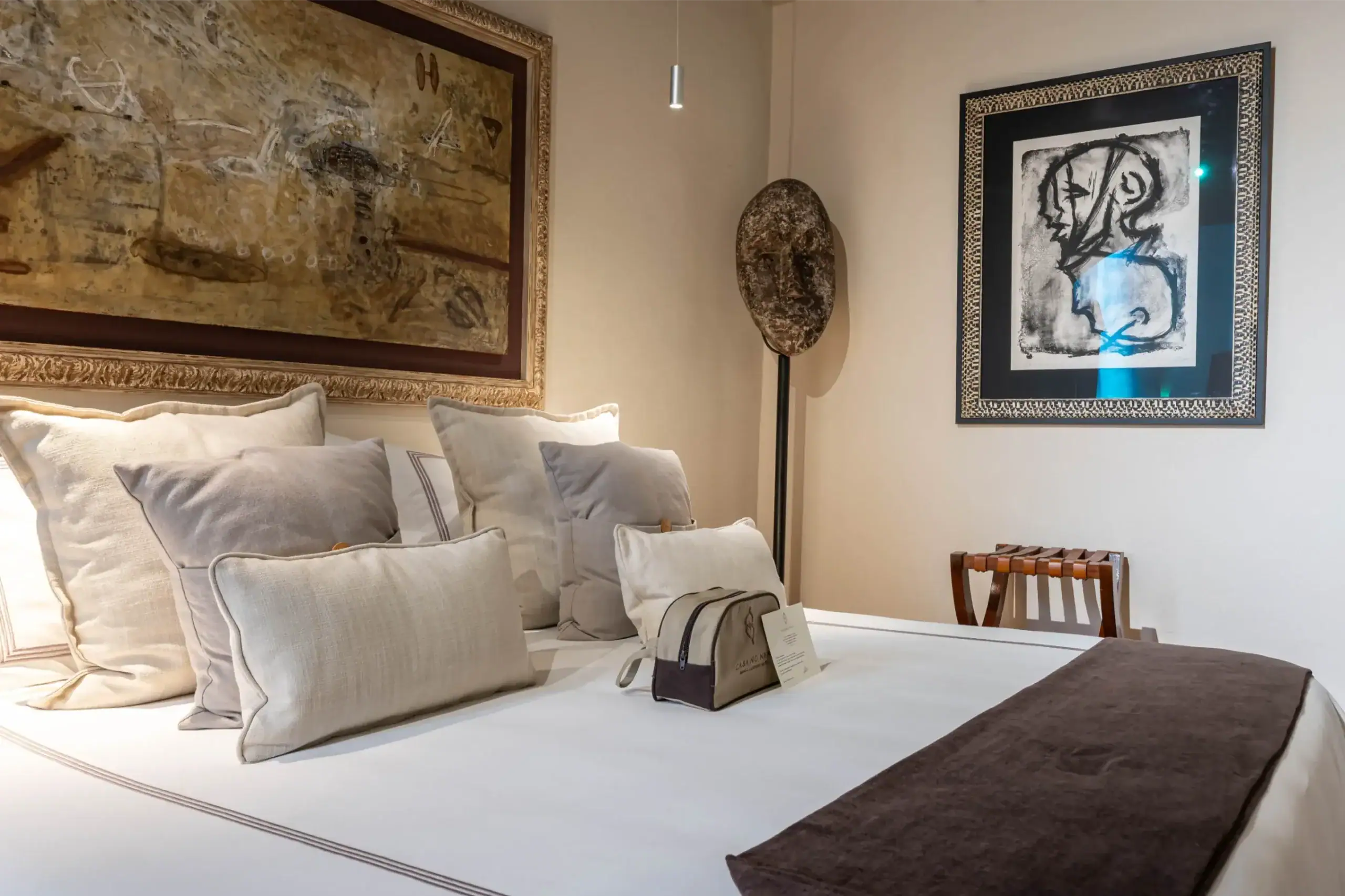 Showroom bedroom with a white bed, beige pillows, and two large framed artworks on opposite walls, San Miguel de Allende