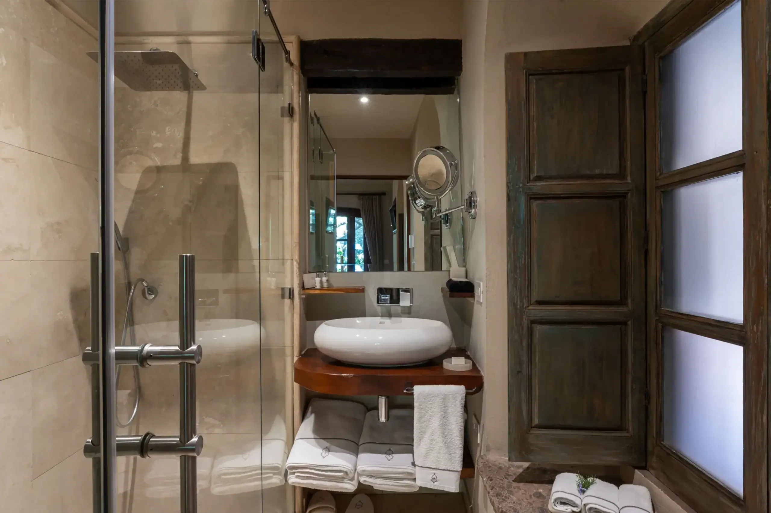 Modern bathroom with glass shower enclosure, round white vessel sink on a wooden counter, and neatly folded towels nearby, San Miguel de Allende