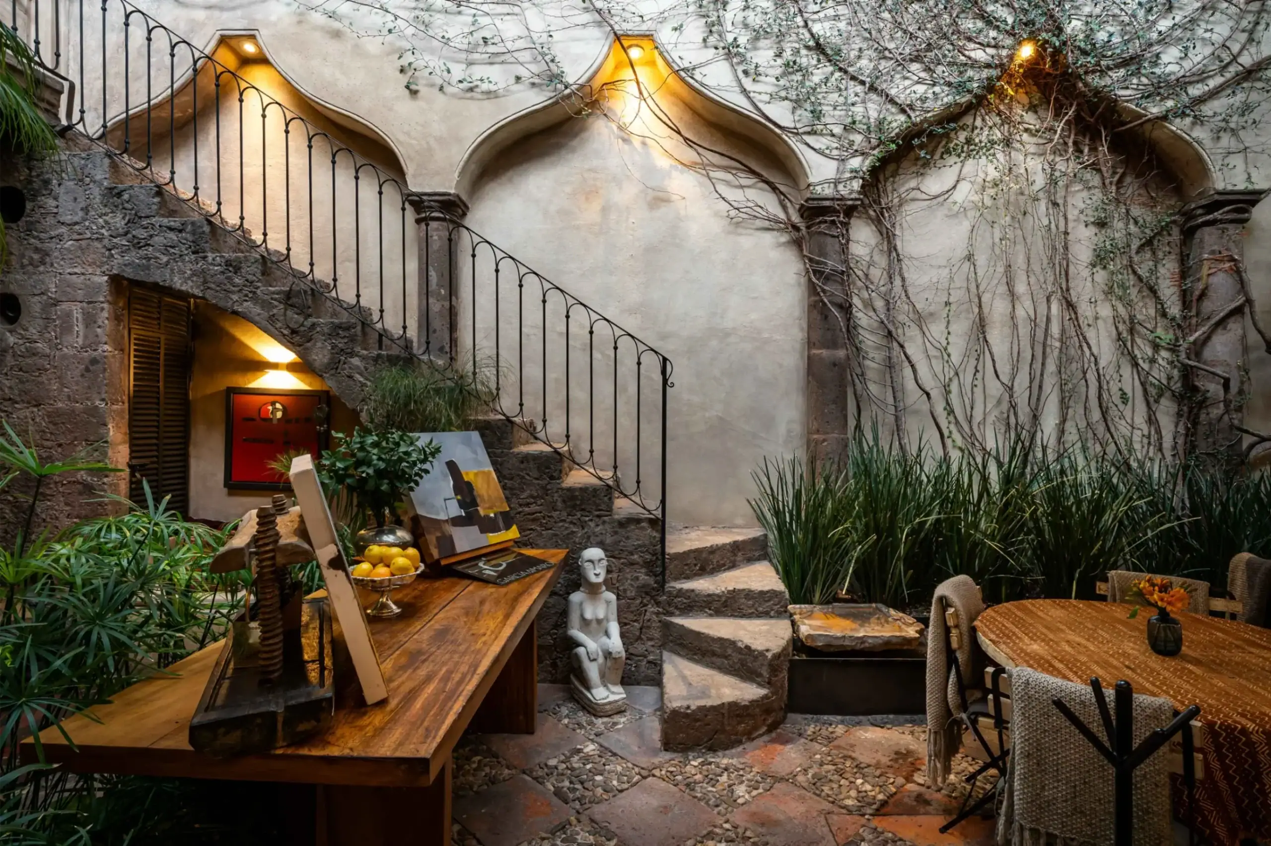 Rustic courtyard dining area with a wooden table, chairs, fruit bowl, and ivy-covered stone walls nearby, San Miguel de Allende