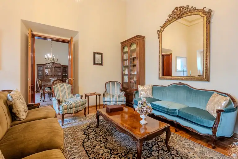 Elegant living room with teal upholstered sofa, striped armchairs, and a large ornate gold mirror on the wall, San Miguel de Allende