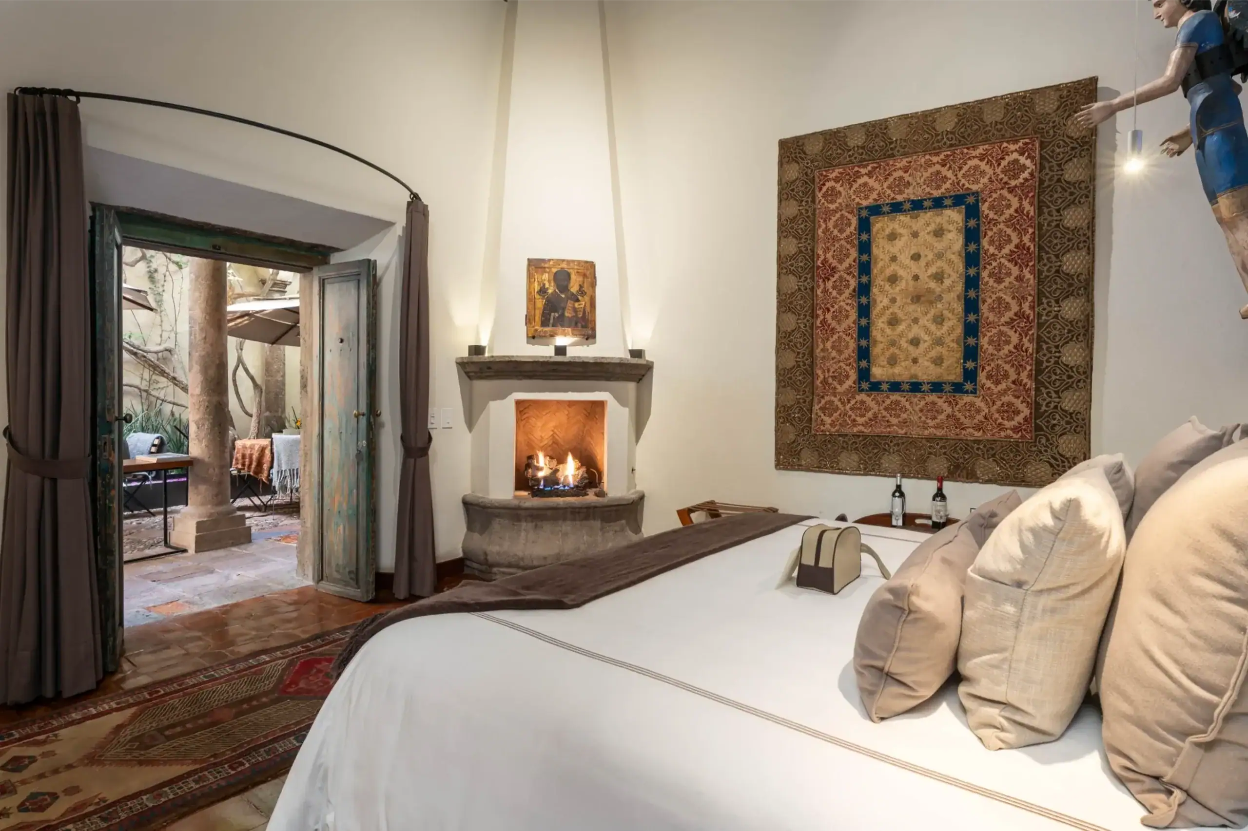 Cozy living room with a lit stone fireplace, small religious icon on the mantel, and a large ornate wall tapestry, San Miguel de Allende