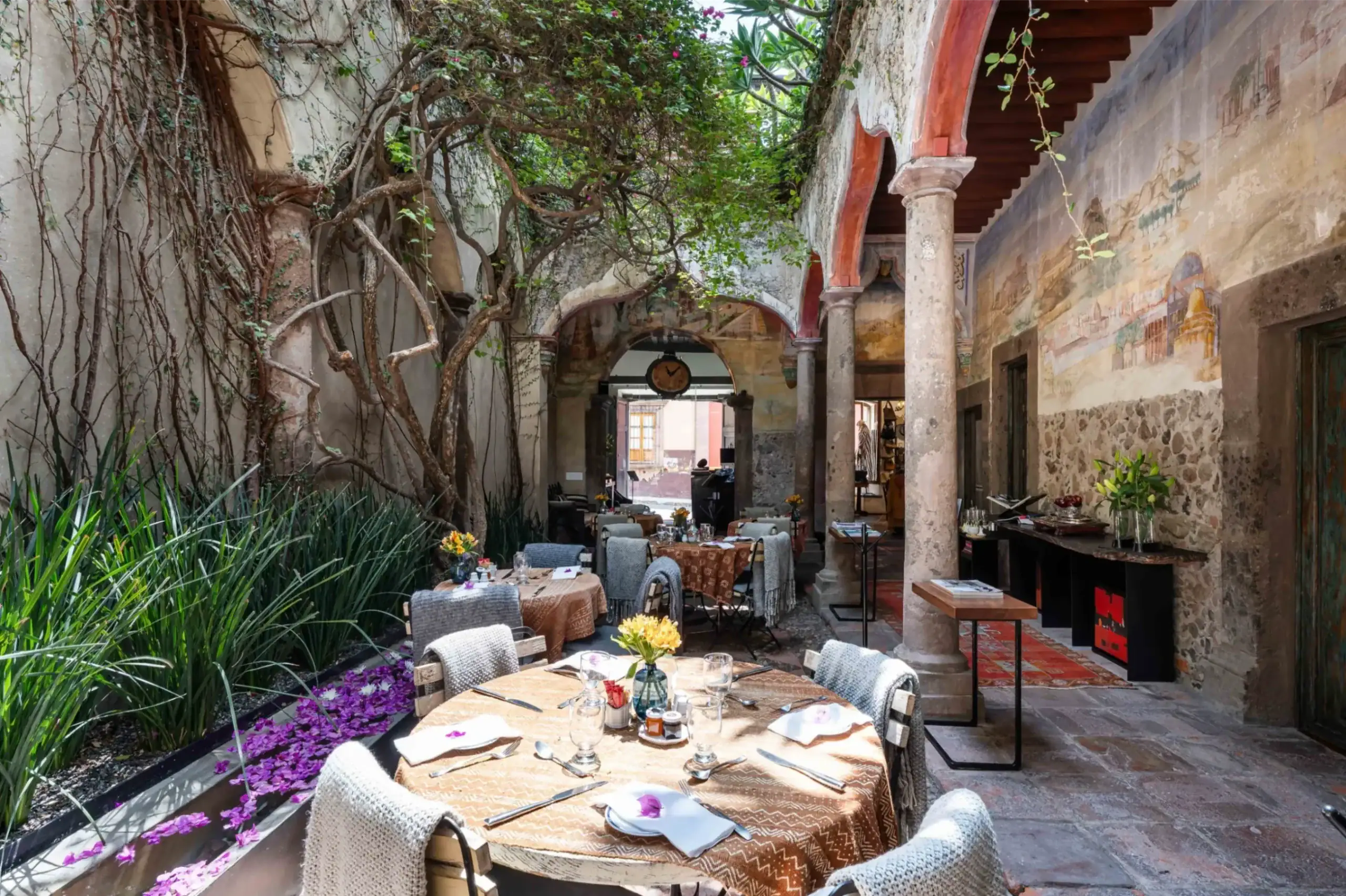 Outdoor dining courtyard with ivy-covered walls, arched red columns, and tables set for a meal under a shaded roof, San Miguel de Allende