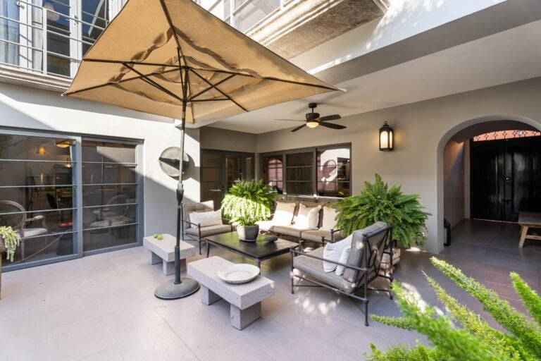 Outdoor patio lounge under a large beige umbrella with cushioned seating and potted ferns, San Miguel de Allende