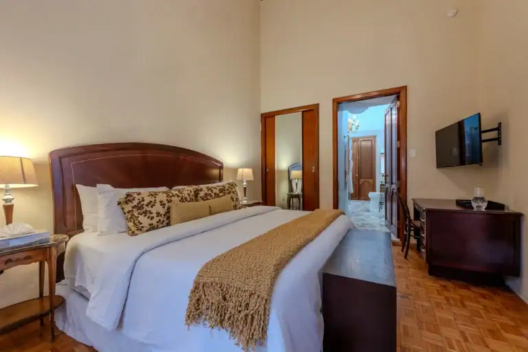 Hotel room with a large bed, decorative pillows, two bedside lamps, and a wall-mounted TV to the right, San Miguel de Allende