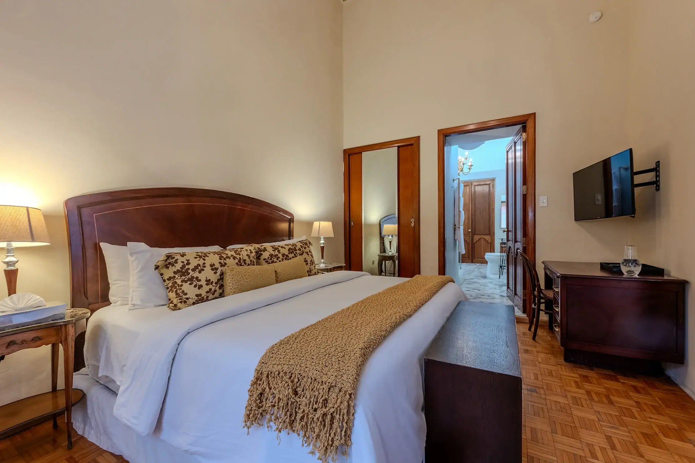 Hotel room with a large bed, decorative pillows, two bedside lamps, and a wall-mounted TV to the right, San Miguel de Allende
