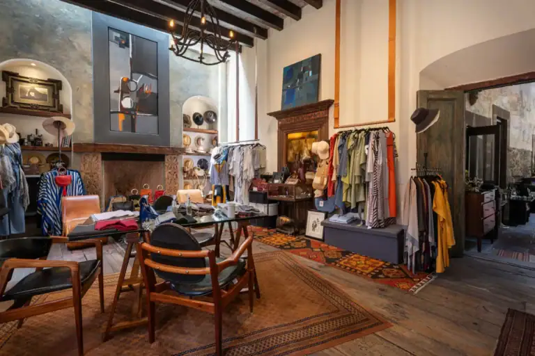 Boutique interior with clothing racks, hats, and accessories displayed around a seating area under warm lighting, San Miguel de Allende