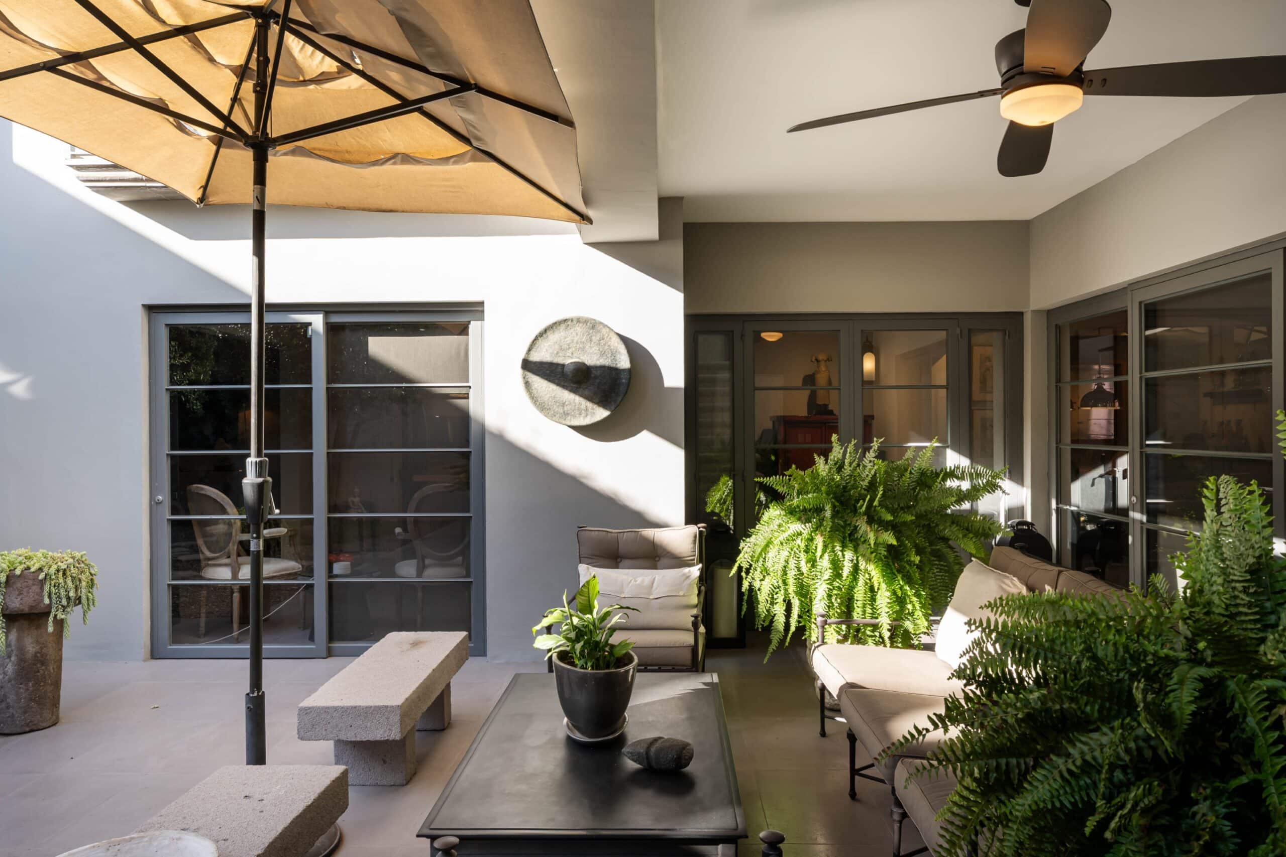 Outdoor patio seating area with beige cushioned chairs, glass coffee table, potted ferns, and a large beige umbrella outside sliding doors, San Miguel de Allende