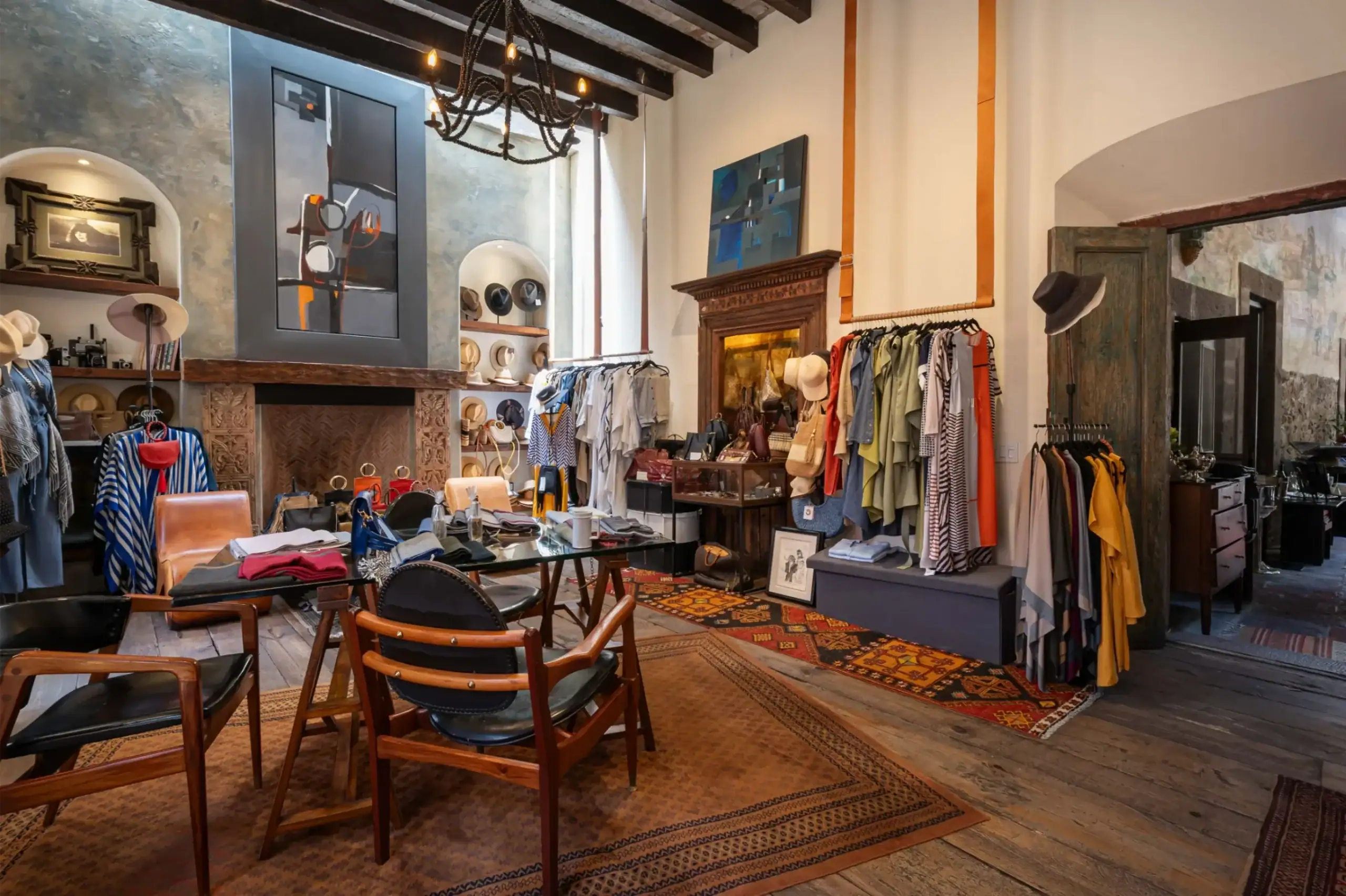 Boutique interior with clothing racks, hats, and accessories displayed around a seating area under warm lighting, San Miguel de Allende