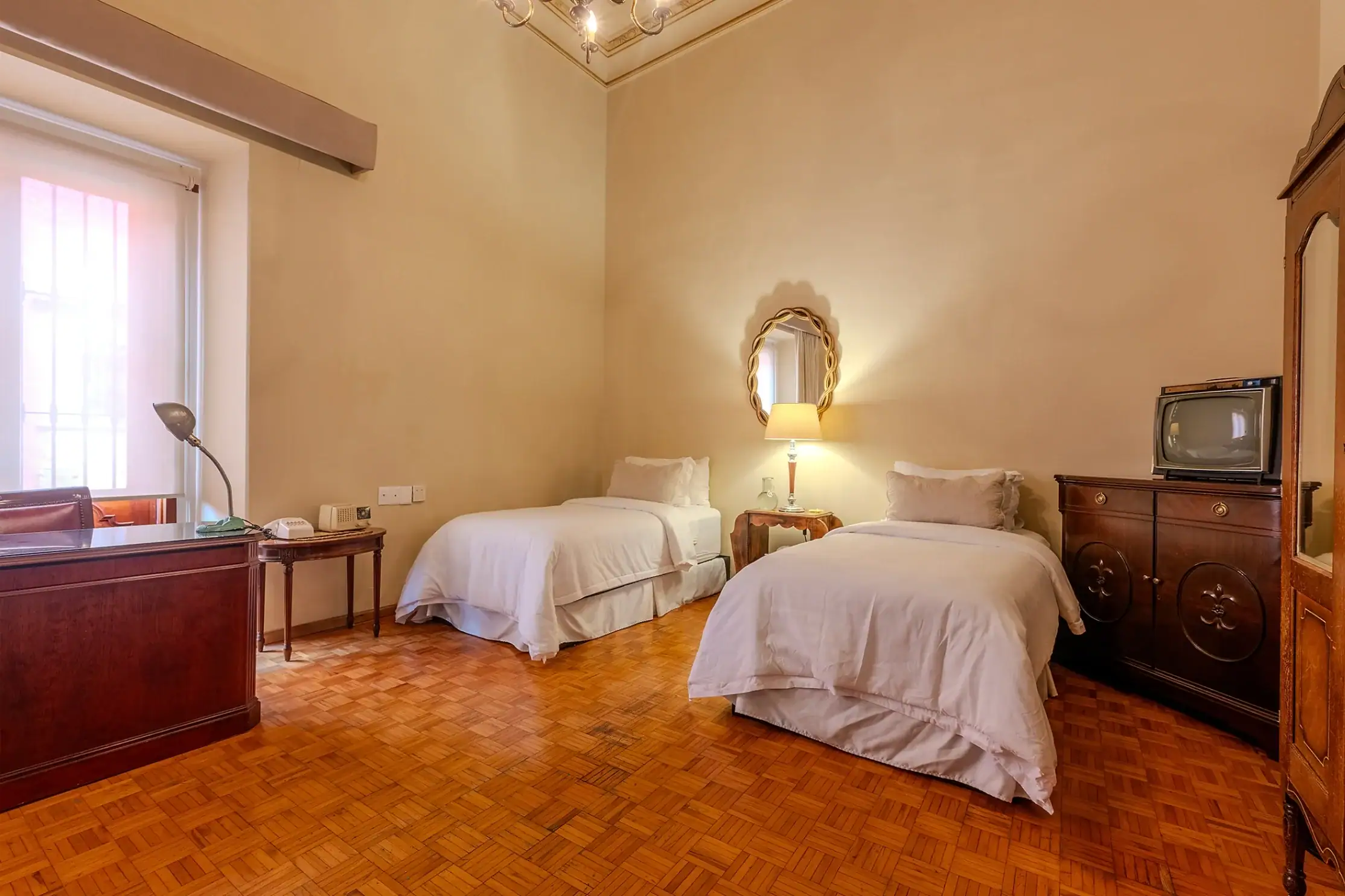 Hotel room with three single beds, wooden dresser, and vintage mirror; warm lighting and parquet floor, San Miguel de Allende