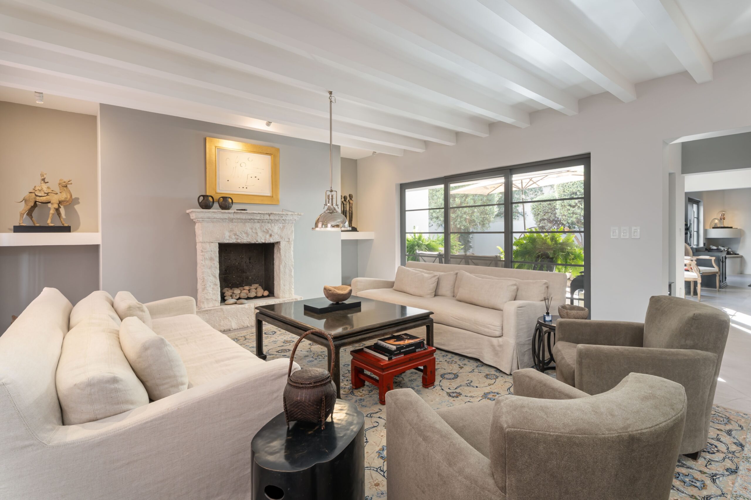 Spacious living room with white beamed ceiling, beige sofas around a dark coffee table, and a stone fireplace, San Miguel de Allende