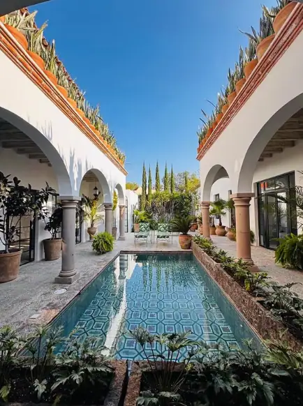 Moorish courtyard with an elongated pool flanked by white arches and columns, potted plants, and a blue sky above, San Miguel de Allende