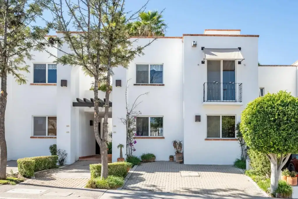 White two-storey condominium building with a paved entrance and trees, San Miguel de Allende