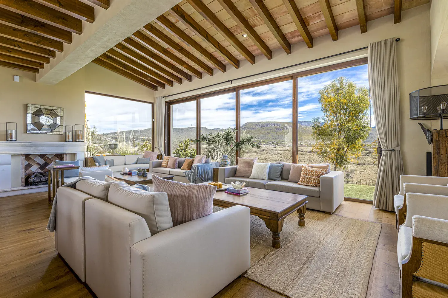 Mañanitas Residence, living room with cream sofas, a fireplace and tall glass doors to the view, San Miguel de Allende