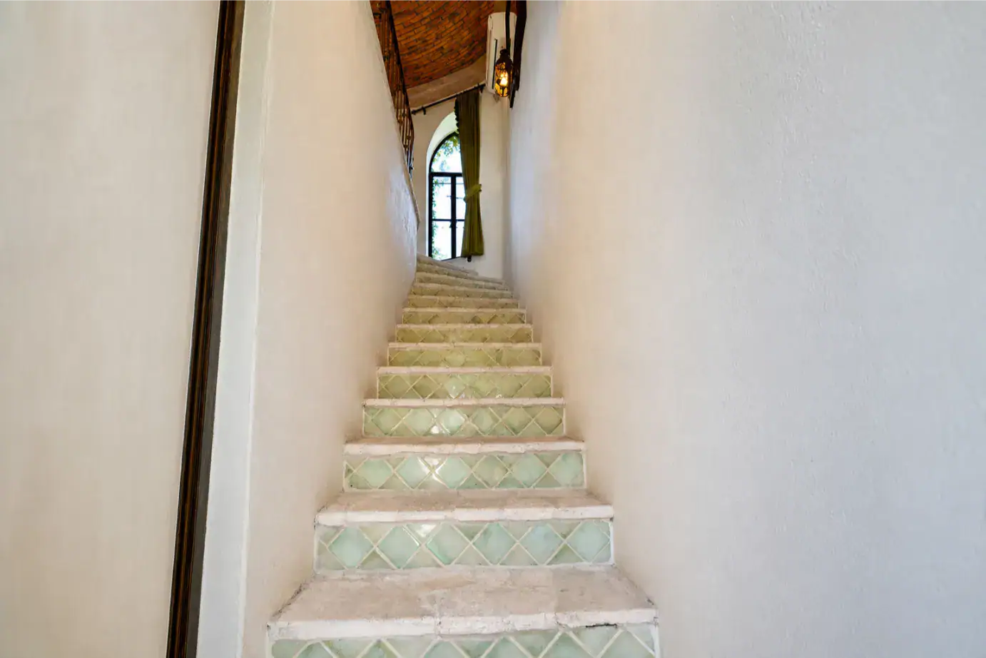 Narrow indoor staircase with pale green tiled risers leading to a window with green curtains at the top, San Miguel de Allende