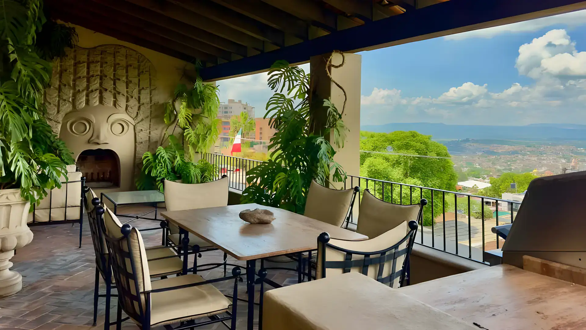 Raíz de las Nubes, covered terrace with a dining table, stone fireplace carving and a view over the town, San Miguel de Allende