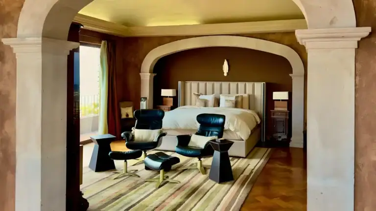 Raíz de las Nubes, bedroom with a tufted headboard, two black leather chairs and arched stone columns, San Miguel de Allende