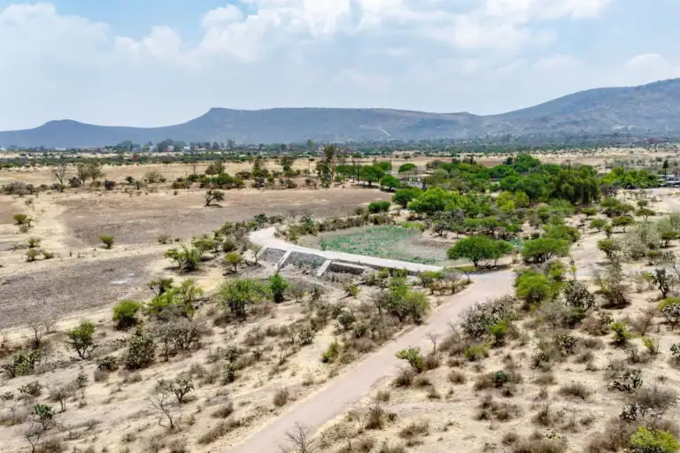 Rancho Guadalupe, aerial view of the land with a curving concrete channel, green trees and hills in the background, San Miguel de Allende