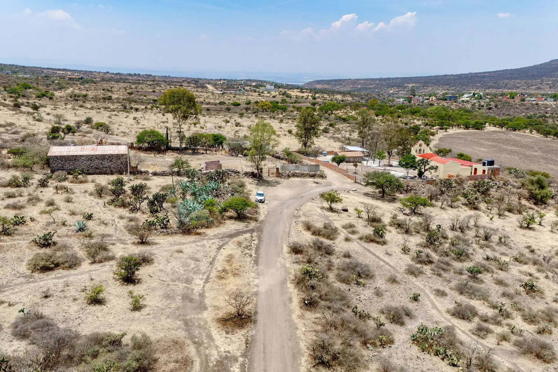 Rancho Guadalupe, aerial view of a dirt track through scrubland past farm buildings and a pickup truck, San Miguel de Allende
