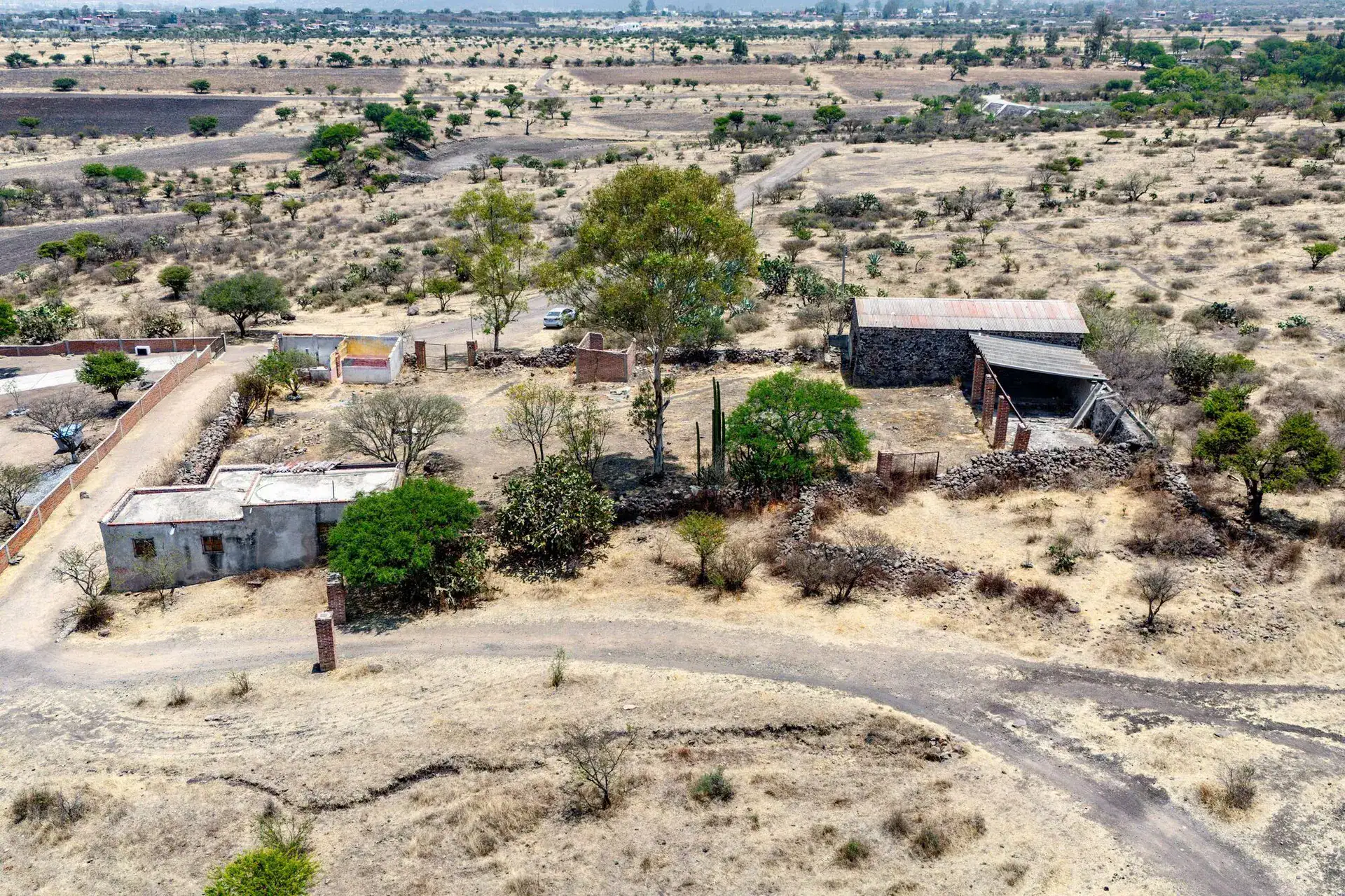 Rancho Guadalupe, aerial view of farm buildings, walls and trees beside a dirt road on the property, San Miguel de Allende