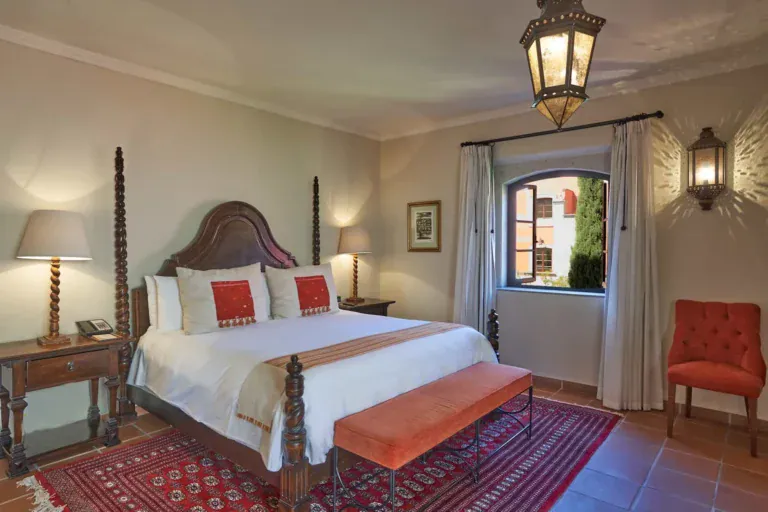 Rosewood Residence 7, primary bedroom with a carved four-poster bed and a red rug, San Miguel de Allende