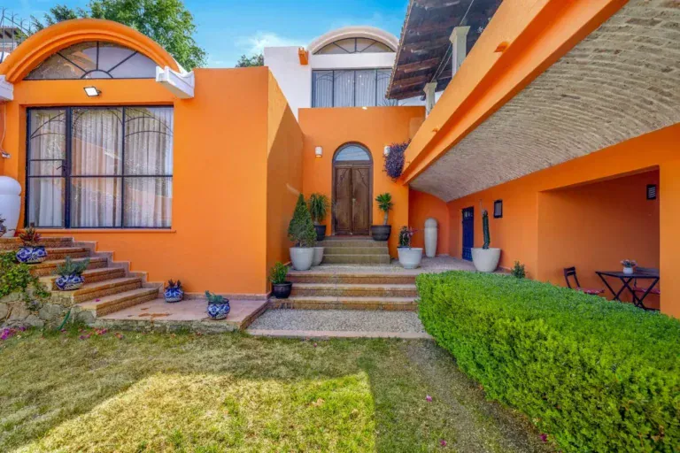 Santo Domingo House, orange house with arched windows, a front staircase, planters and a trimmed hedge above a lawn, San Miguel de Allende