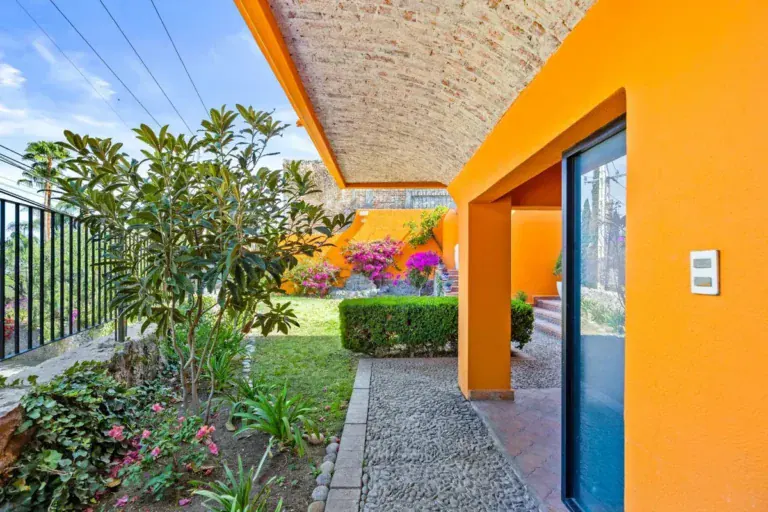 Santo Domingo House, orange facade with a brick vaulted overhang, a glass door and a flowering garden, San Miguel de Allende