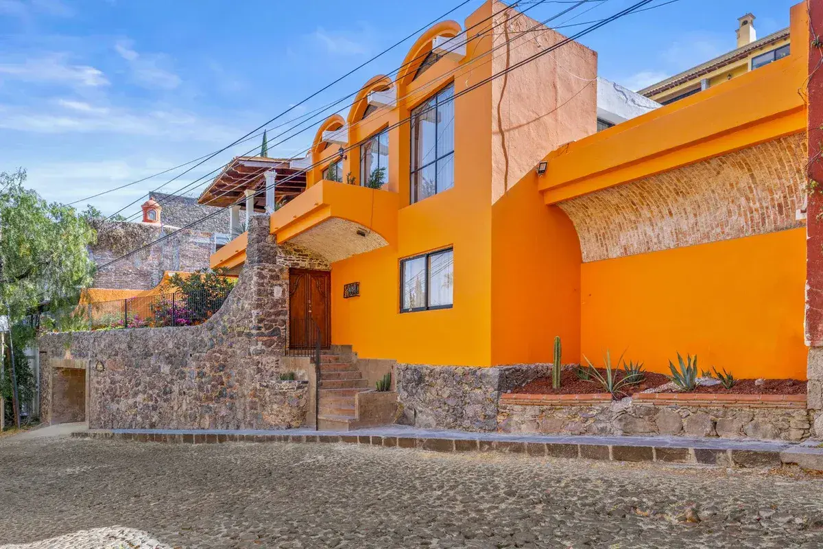 Santo Domingo House, orange multi-level house with arched balconies and a stone retaining wall on a cobblestone lane, San Miguel de Allende