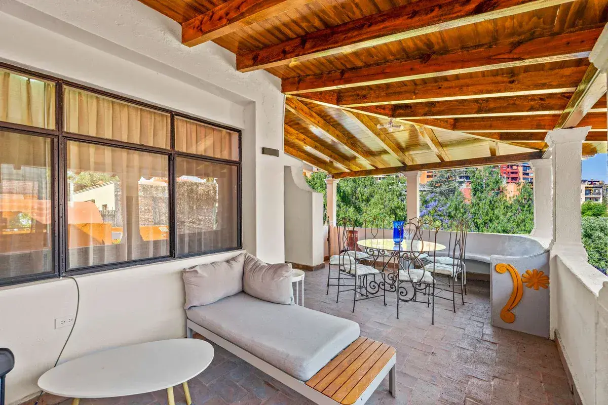 Santo Domingo House, covered terrace with a wood beam ceiling, a daybed and a wrought iron dining set, San Miguel de Allende