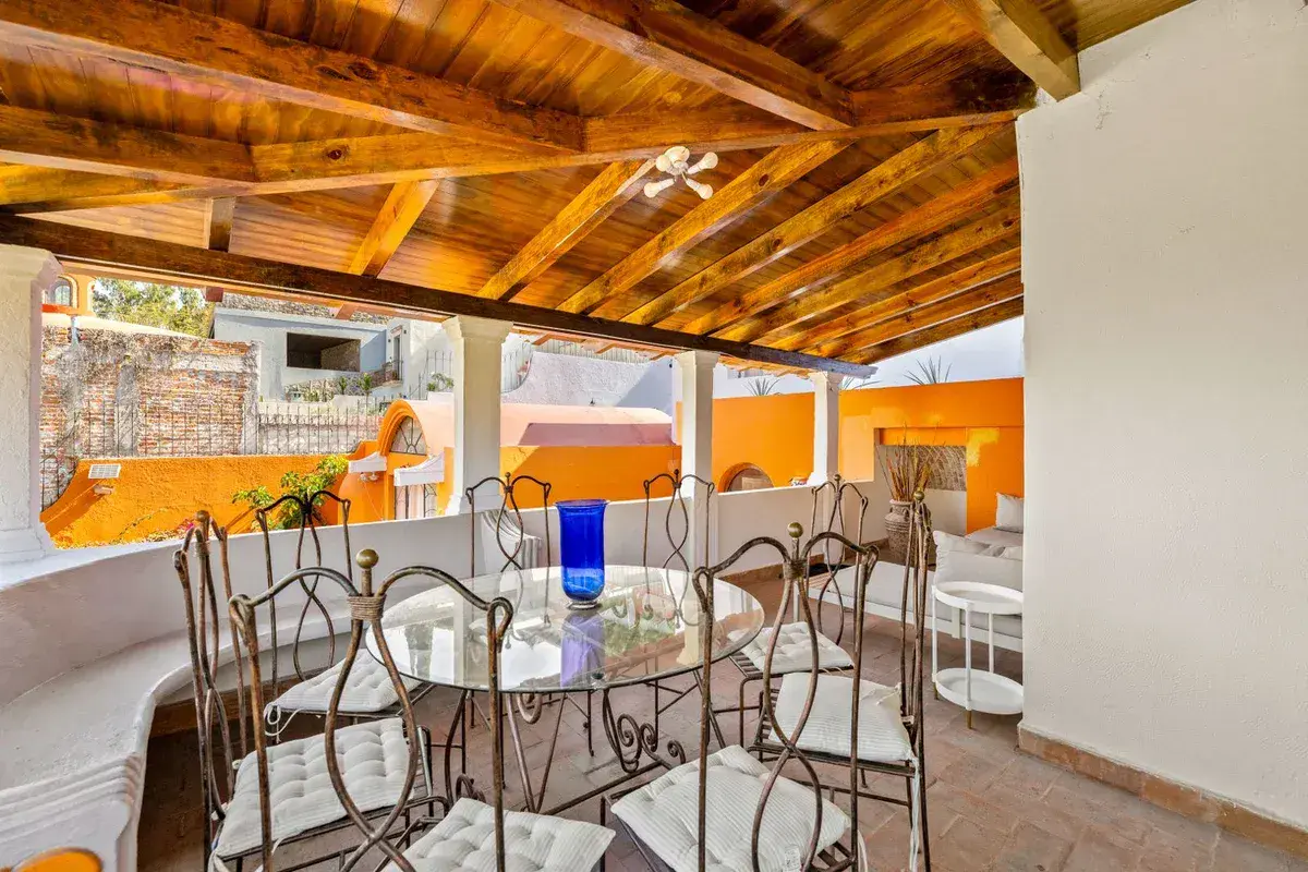 Santo Domingo House, covered terrace with a round glass-top dining table and iron chairs under wood beams, San Miguel de Allende