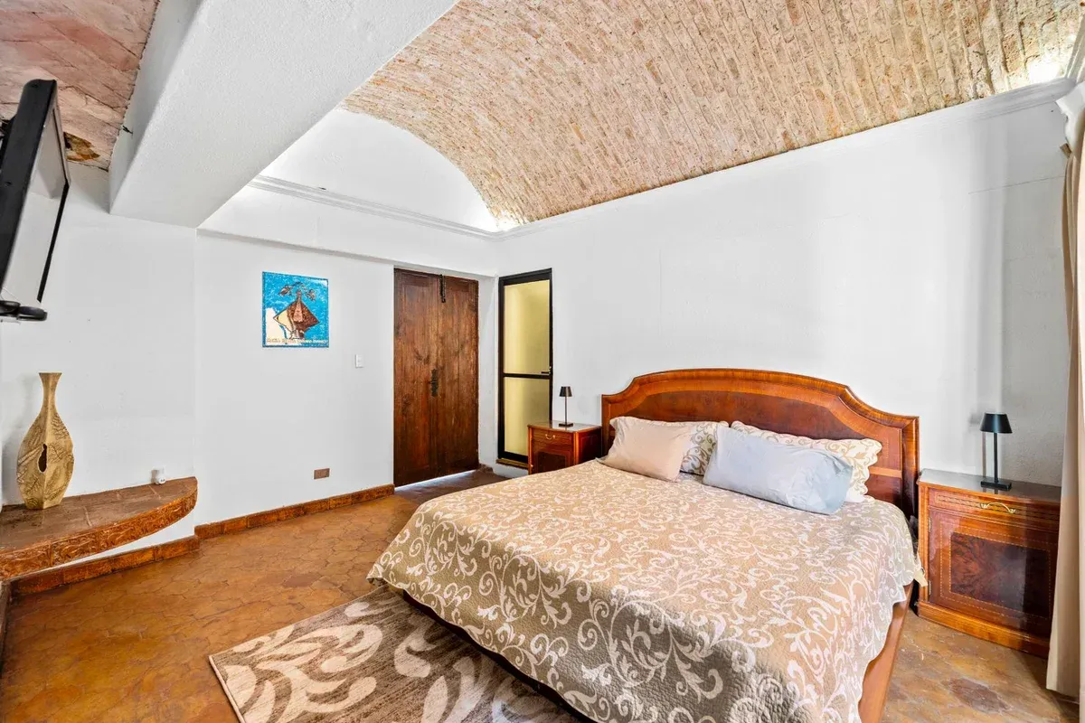 Santo Domingo House, bedroom with a carved wood headboard, a patterned bedspread and a brick vaulted ceiling, San Miguel de Allende