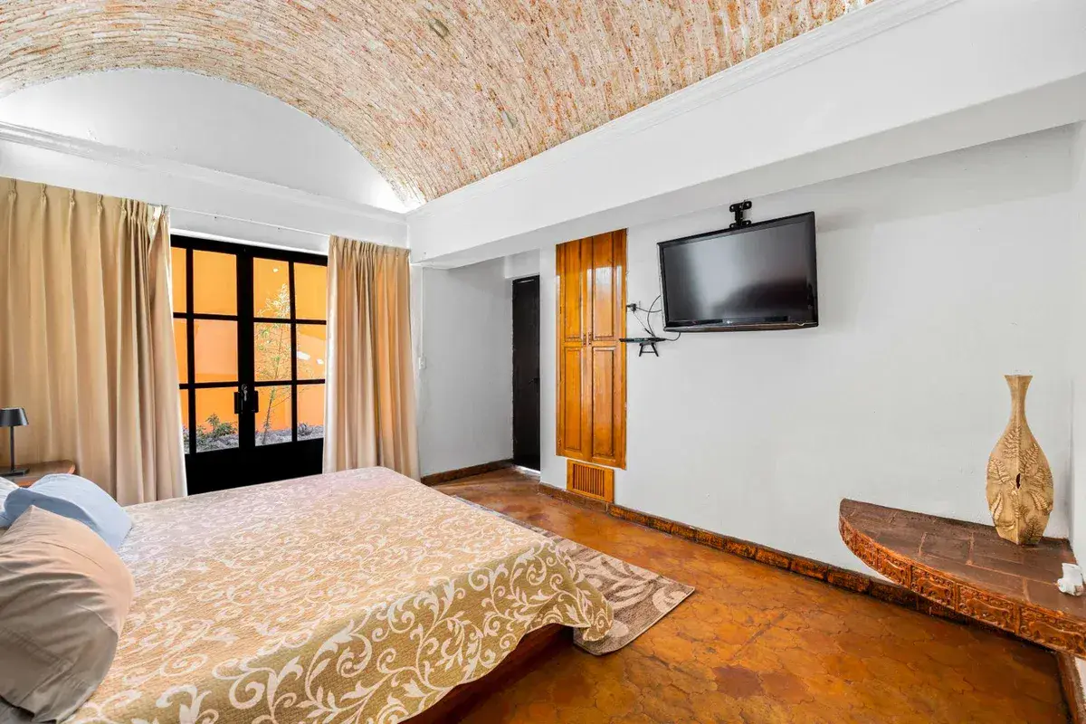 Santo Domingo House, bedroom with a patterned bedspread, a wall-mounted television and glass doors with curtains, San Miguel de Allende