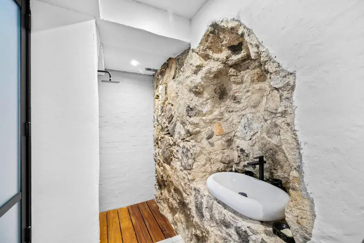 Santo Domingo House, shower with a natural rock wall, a stone vessel sink and a wood deck floor, San Miguel de Allende
