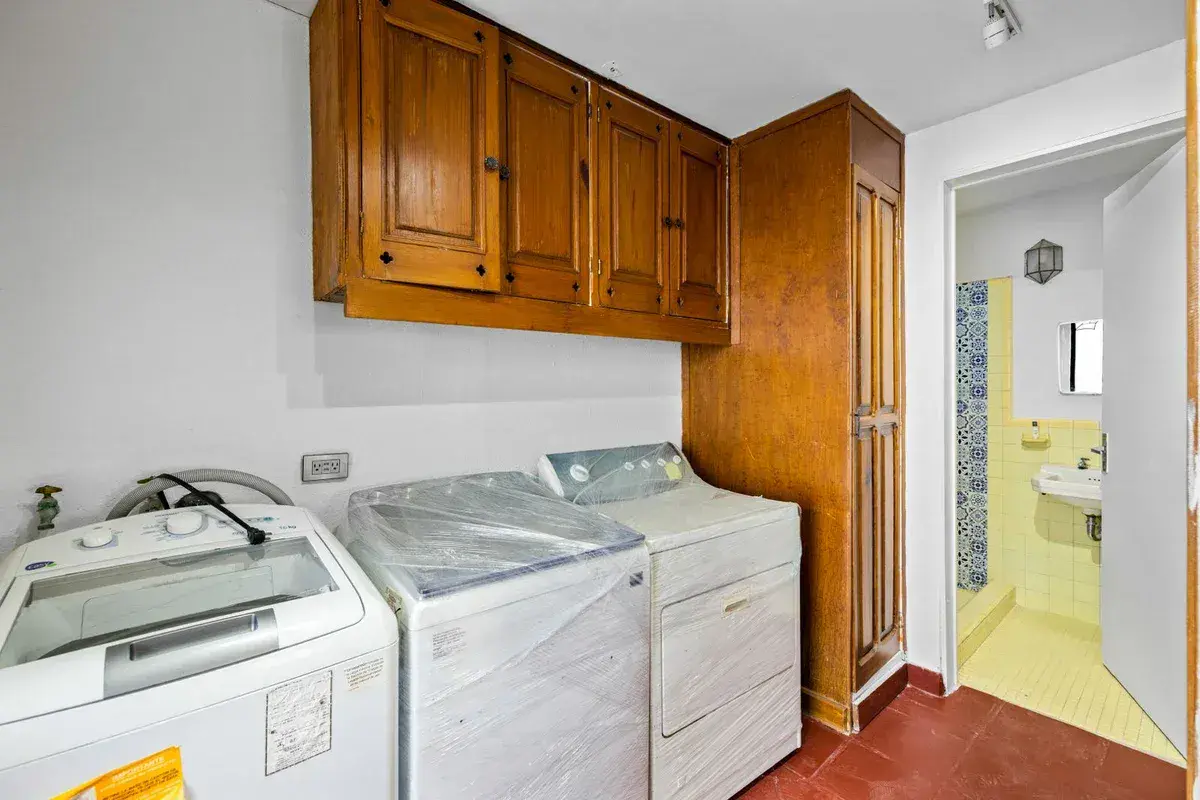 Santo Domingo House, laundry room with a washer and dryer, wood cabinets and a tiled bathroom beyond, San Miguel de Allende