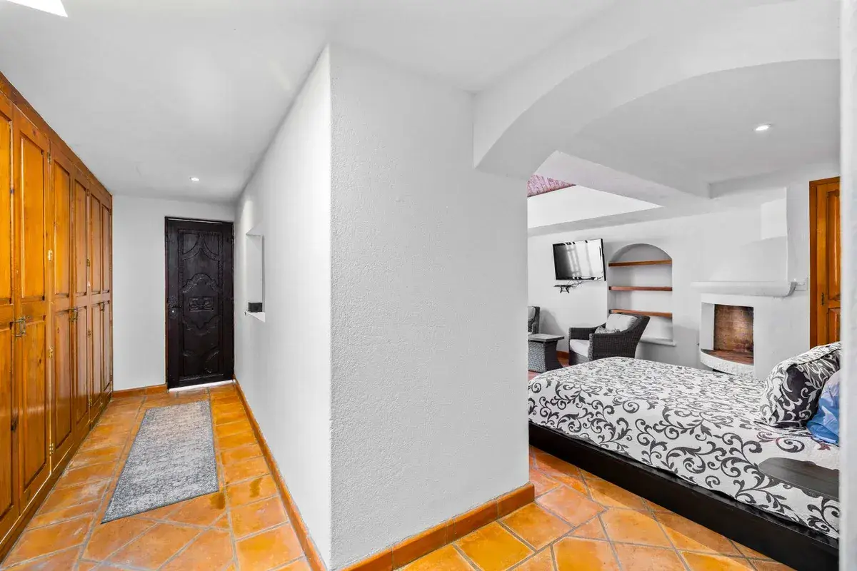 Santo Domingo House, hallway with wood closet doors and a bedroom with a fireplace beyond, San Miguel de Allende