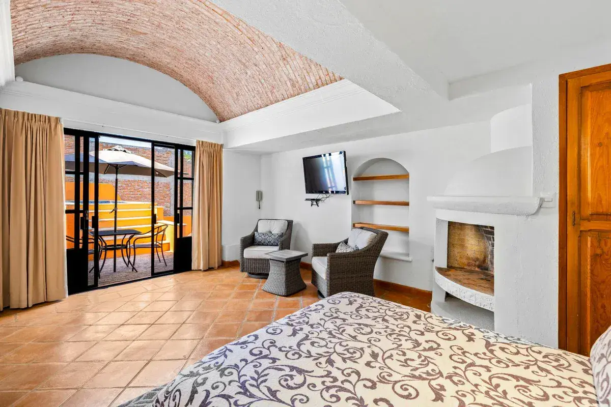 Santo Domingo House, bedroom with a patterned bed, a corner fireplace, armchairs and glass doors to a terrace, San Miguel de Allende